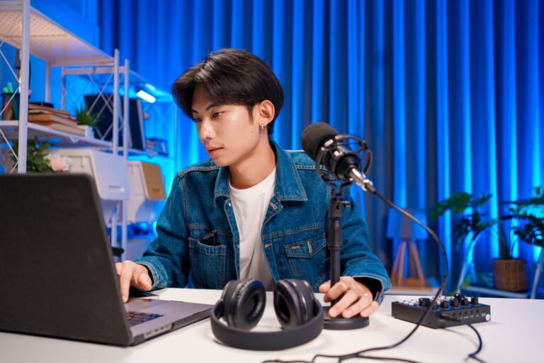 Podcast host preparing recording equipment while looking at a laptop for a remote interview